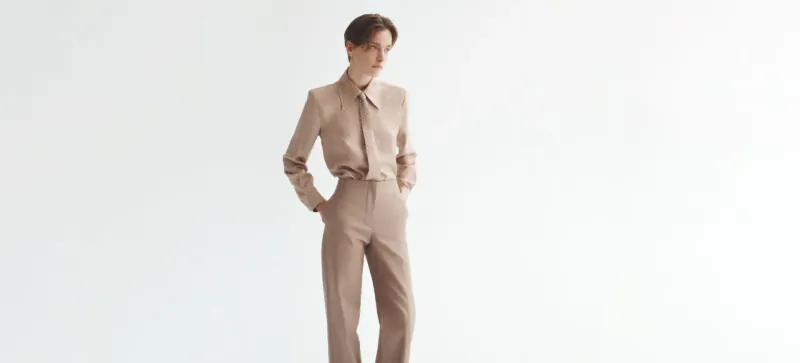 Model in beige Scanlan Theodore suit, hands in pockets, standing confidently against white background