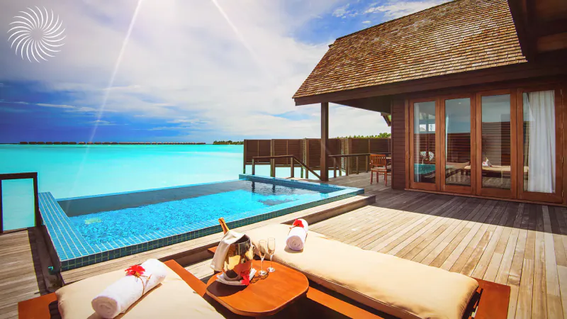 Luxury overwater villa at Hideaway Beach Resort with infinity pool, turquoise lagoon, sun loungers, towels, and champagne on deck.