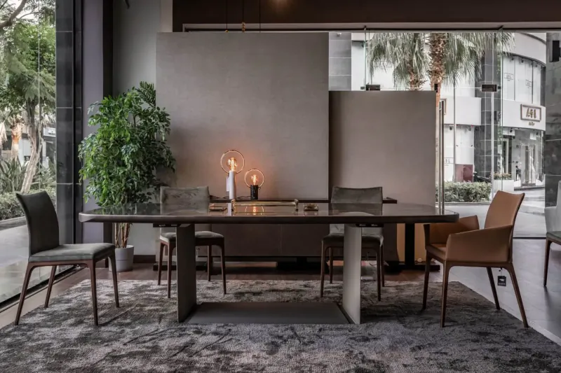 Modern wooden dining table with chairs in elegant showroom, potted plant, lit candle, large windows to palm trees