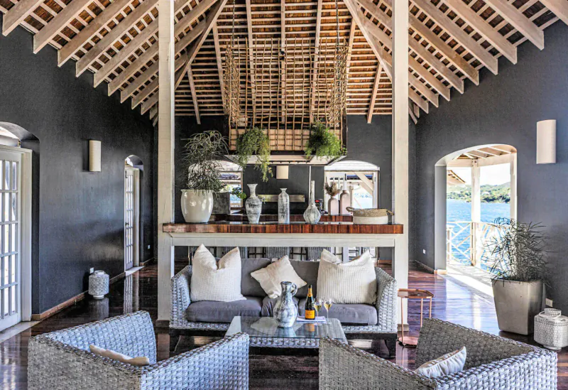 Spacious open-plan living area at Rokuni Antigua with wooden beamed ceiling, white sofas, potted plants around central table, lake view.