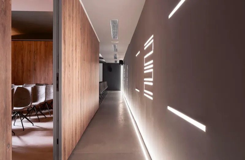 Modern hotel hallway with wooden walls, chairs in meeting room, linear LED lights on gray walls, Elysium Boutique Hotel Crete.