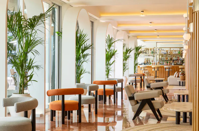 Elegant Hotel Riomar lounge in Ibiza with arched windows, potted palms, modern orange and gray chairs, and stylish bar.