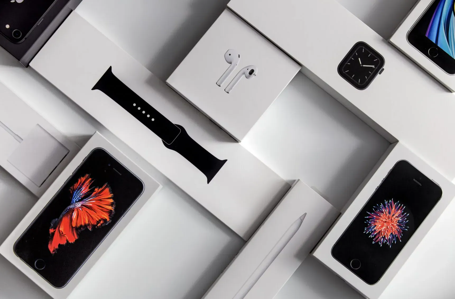 Arranged Apple products: iPhone boxes with orange screens, AirPods, Apple Watch, black band on white background