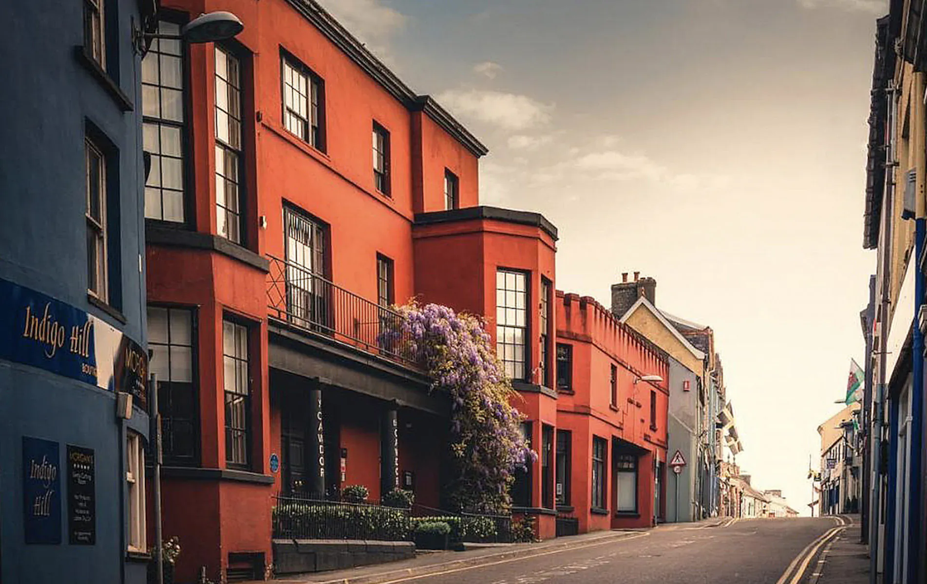 Colorful terraced buildings with red facades, purple flowers, and 'Cawdor' sign on a quiet street in Llandeilo, Wales