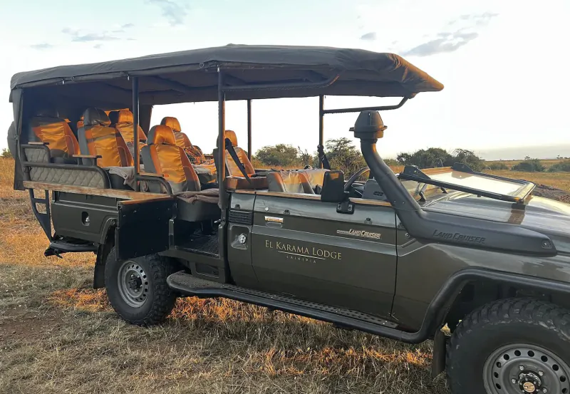 El Karama Lodge safari Land Cruiser with orange seats parked on golden savanna at sunset