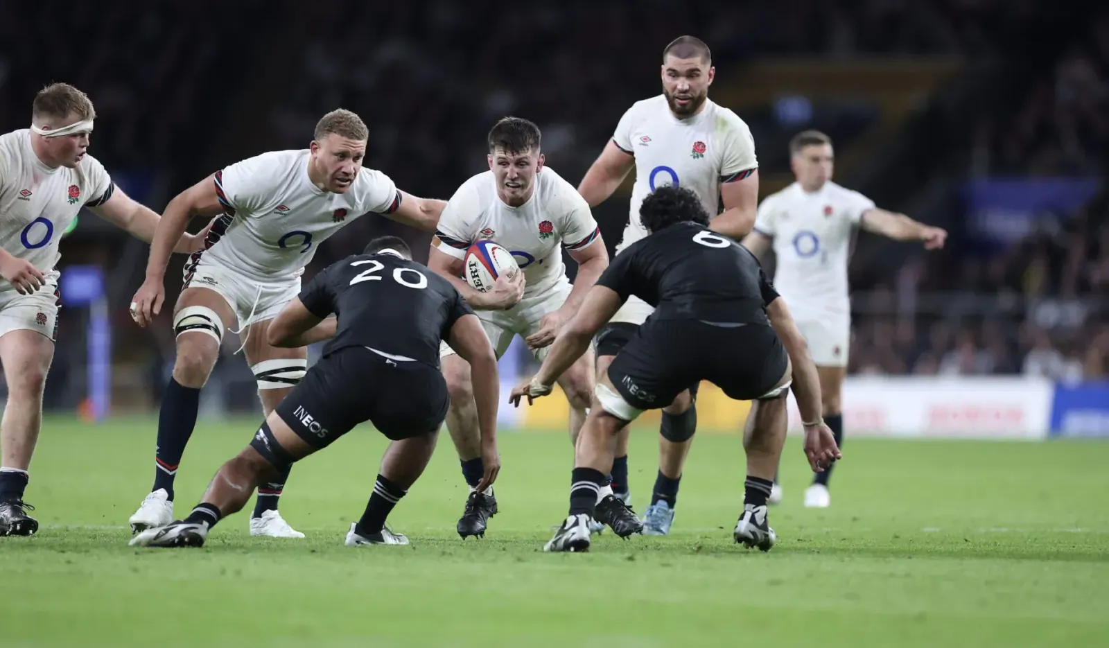 England white vs New Zealand black rugby players in intense tackle scrum on green field, player 20 holds ball