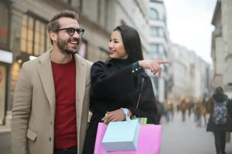 Smiling man and woman with shopping bags on city street; she points ahead, evoking spring renewal.