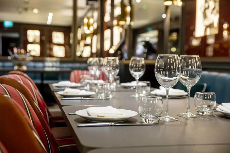 Elegant restaurant table set with wine glasses, plates, and napkins in warm, mirrored interior