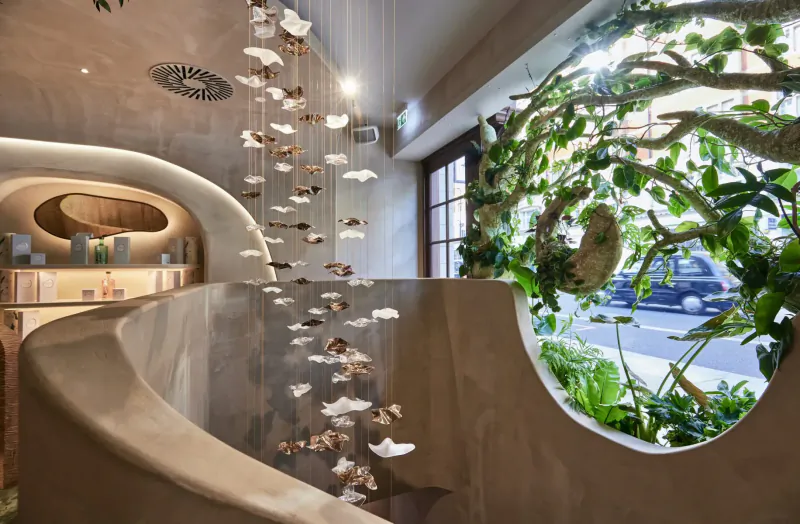 HVN Knightsbridge wellness centre gallery: curved beige staircase with hanging white flower sculptures and lush green plants framing window view.