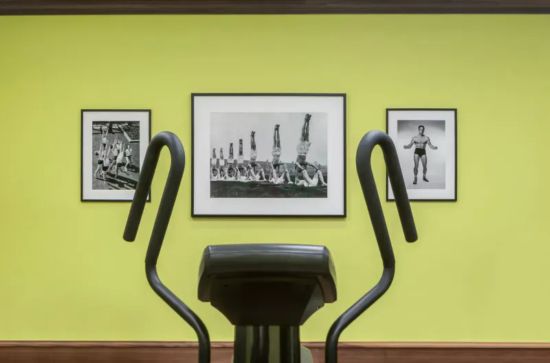 Black-and-white photos of children on gymnastics rings flank a stationary bike against a lime green wall in El Llorenç Parc de la Mar gallery.