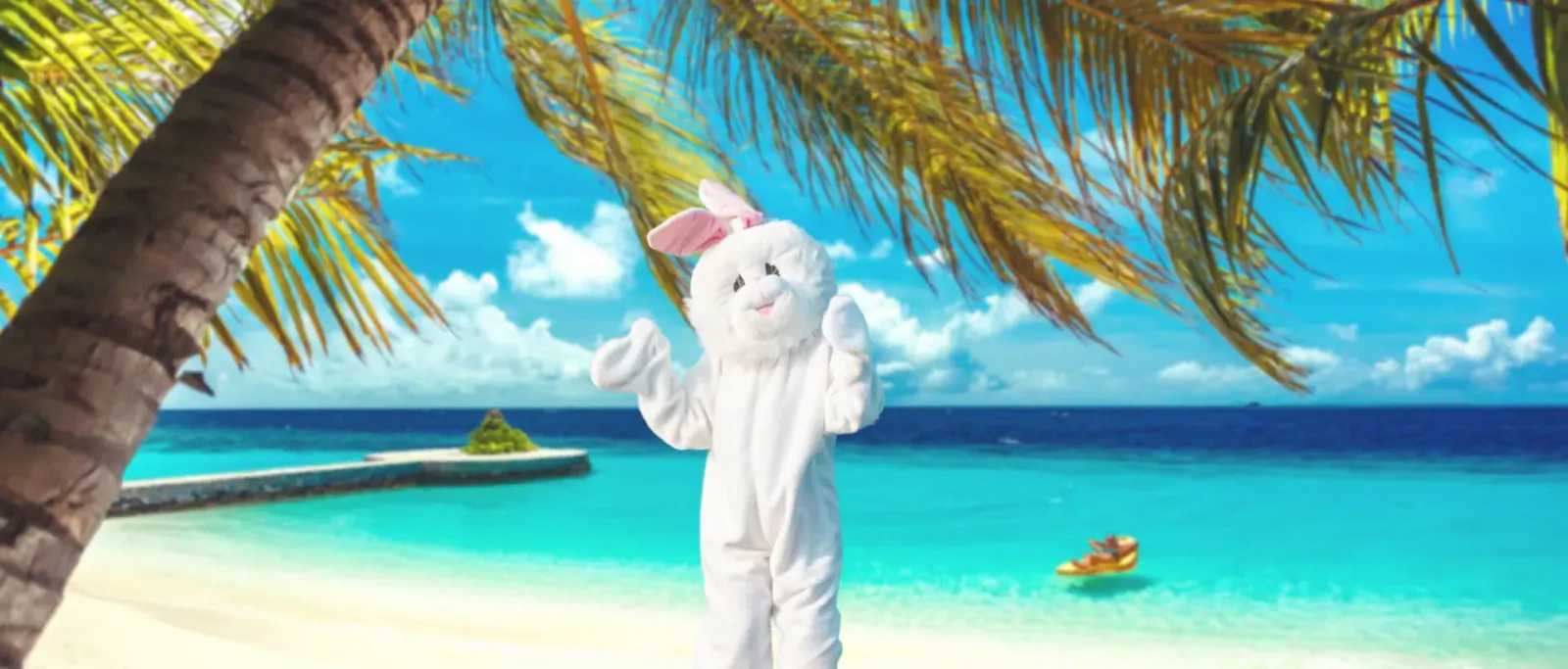 White bunny mascot posing with arms raised on tropical beach at Lily Beach Resort, palm trees and turquoise ocean backdrop