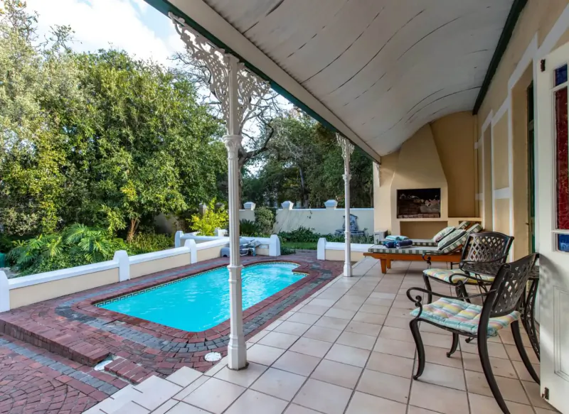 Evergreen Manor and Spa's covered veranda with turquoise pool, braai, cushioned chairs, and lush garden view in Stellenbosch.