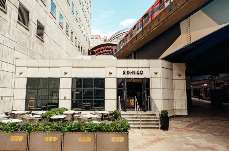 Franco restaurant exterior at Six by Nico Canary Wharf with outdoor seating under elevated train tracks