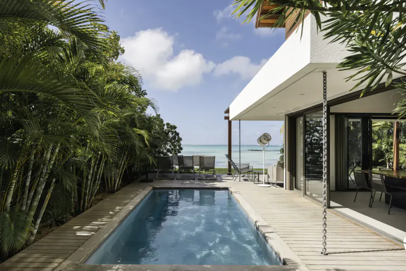 Modern Villa Sapphire with infinity pool, lounge chairs, tropical palms, and ocean view in Belle Mare, Mauritius.