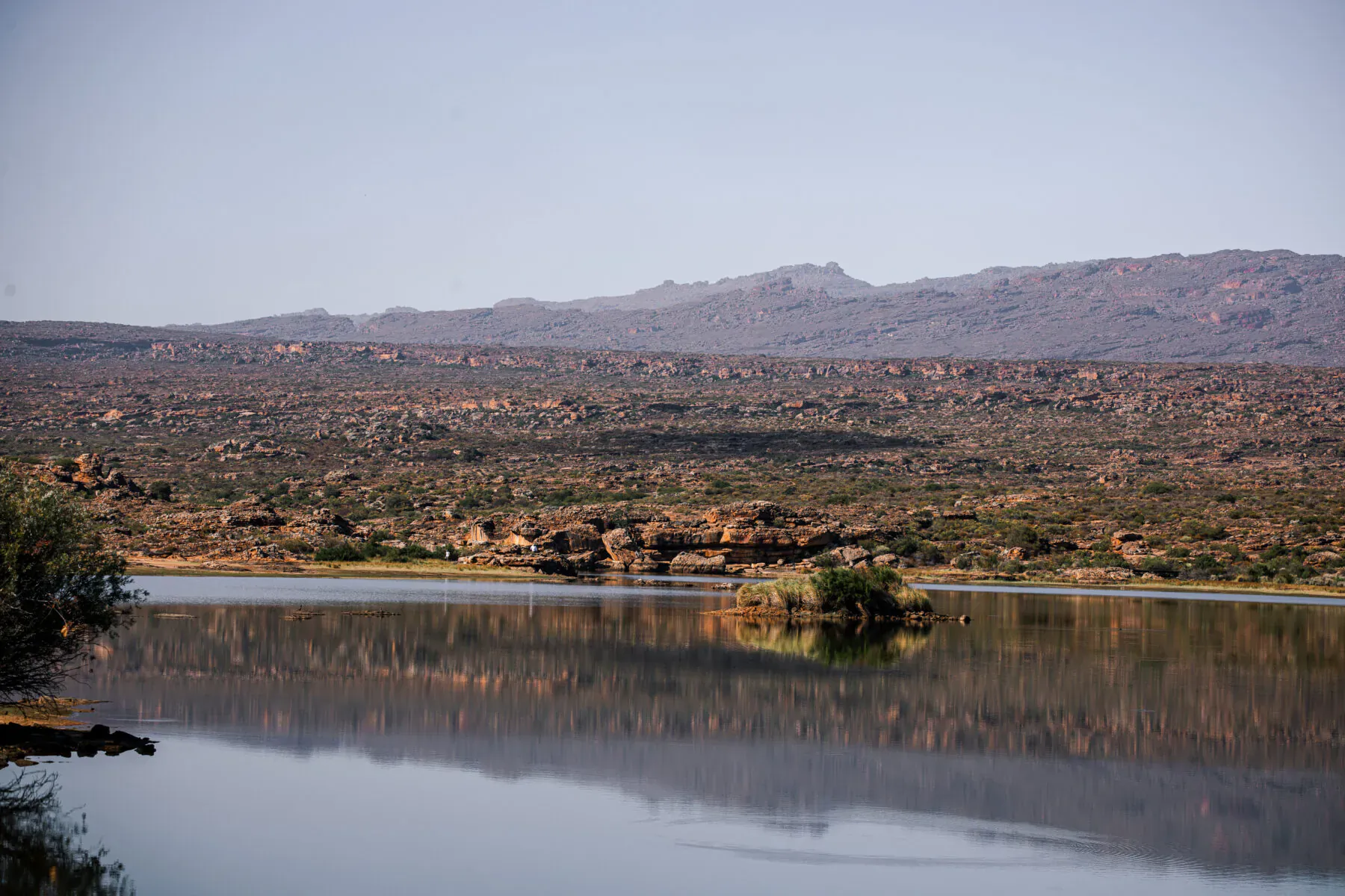 Serene lake reflecting rugged mountains and rocky bushveld in Bushman’s Kloof wilderness.