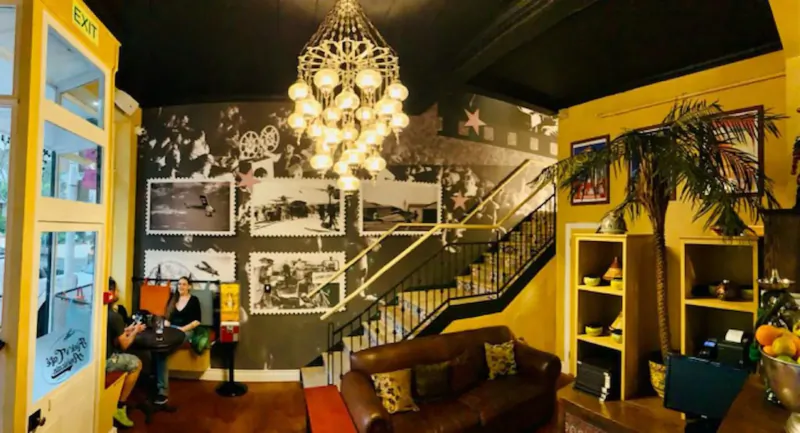 Cozy Kloof Street gallery interior in Cape Town with yellow walls, chandelier, black-and-white photos, stairs, leather sofa, plants, and patrons.