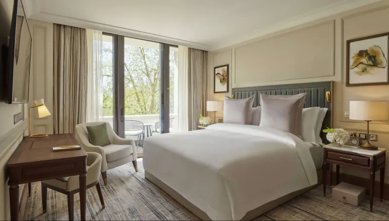 Elegant Carlton Tower Jumeirah hotel room in London with king bed, desk, lamps, and balcony view of trees.