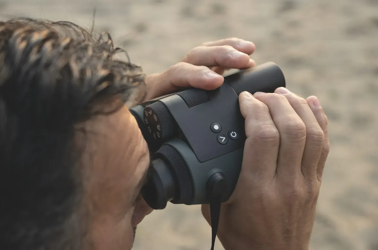 Man using Swarovski smart binoculars with buttons and strap on sandy beach