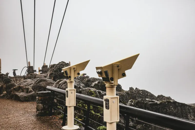 Two coin-operated binoculars on a rocky overlook railing at Cape Town Aerial Cableway in misty weather