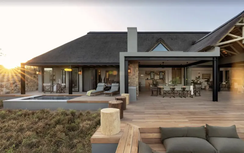 Monwana Game Lodge's modern thatched eco-lodge at sunset, with infinity pool, deck, lounge seating, and dining area overlooking savanna.