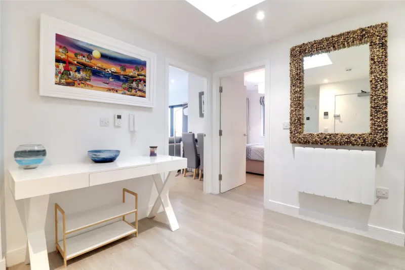 Bright hotel hallway with white X-frame console table, blue bowls, colorful sunset painting, and gold mirror.