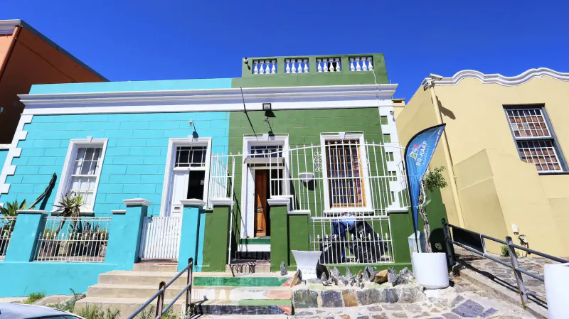 Colorful Cape Malay houses in blue, green, and yellow with plants and railings under blue sky