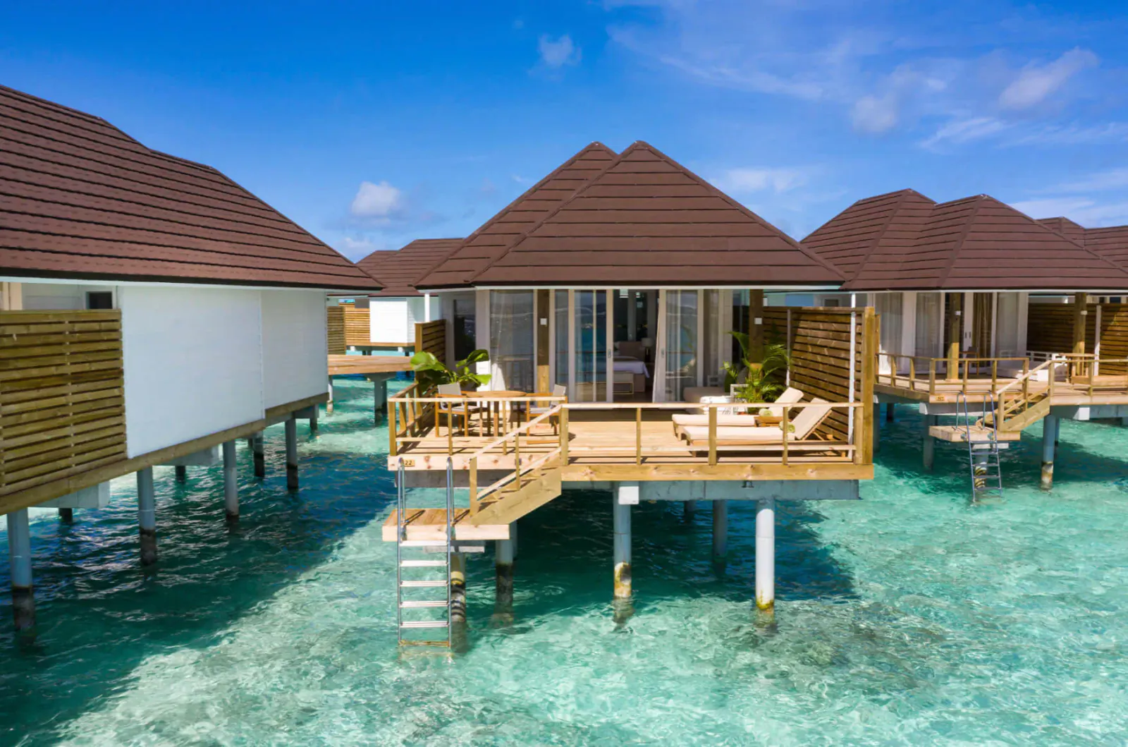 Luxury overwater villas with wooden decks, loungers, and stairs, on turquoise lagoon under blue sky