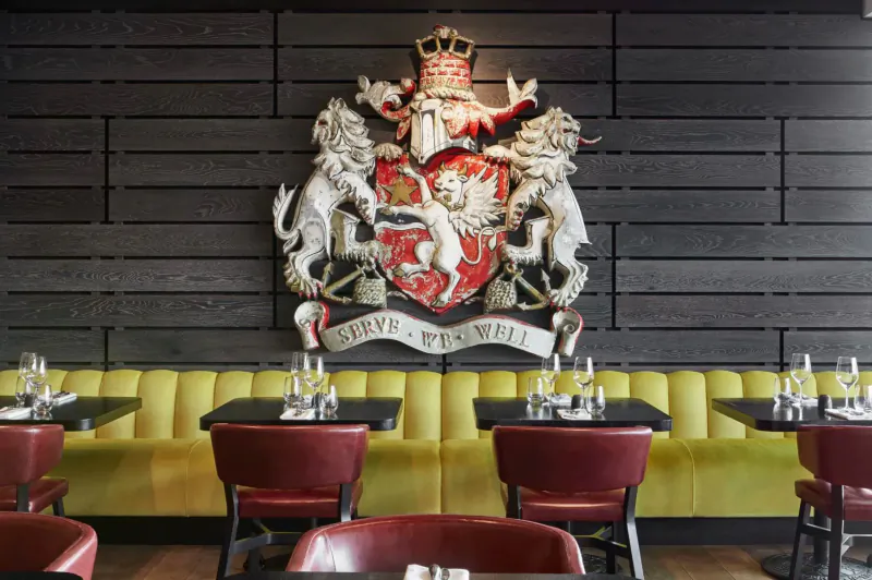 Coat of arms with lions, crown, and 'Sea & Well' motto on black wall above yellow banquette seating and tables in spa lounge