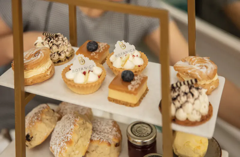 Three-tiered stand of luxury afternoon tea pastries, scones, tarts, cream puffs, and jam at elegant hotel.
