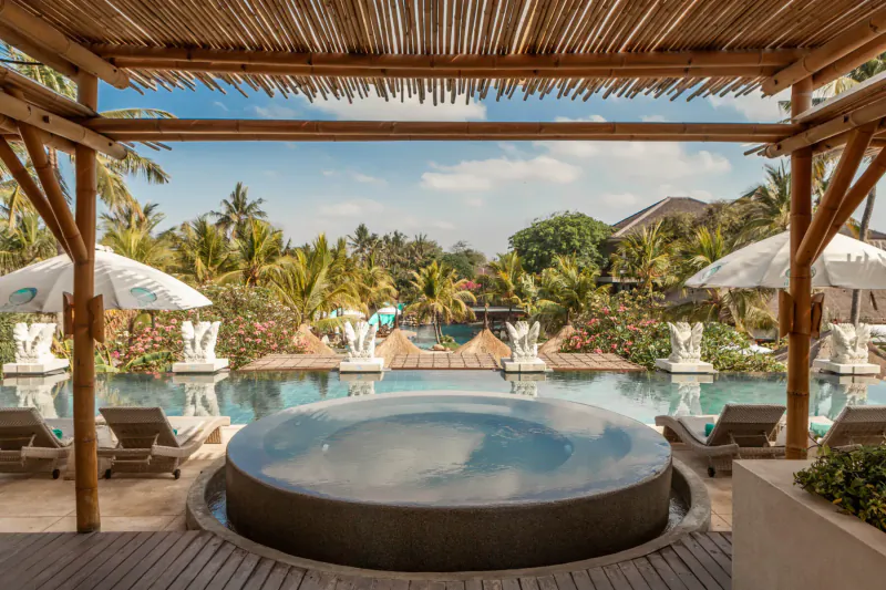 Azul Beach Club Bali: Tropical infinity pool, jacuzzi, loungers, umbrellas, and palm trees under bamboo pavilion.