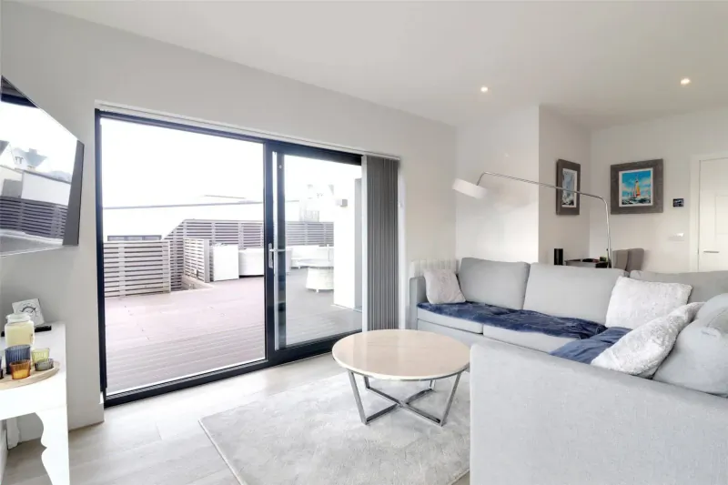 Modern living room in Woolacombe Bay stay with grey sofa, round table, open sliding doors to deck and sea view.