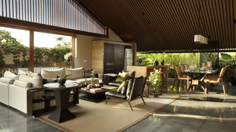 Spacious open-plan living and dining area in Amétis Villa Bali, with white sofas, wooden accents, plants, and garden view.