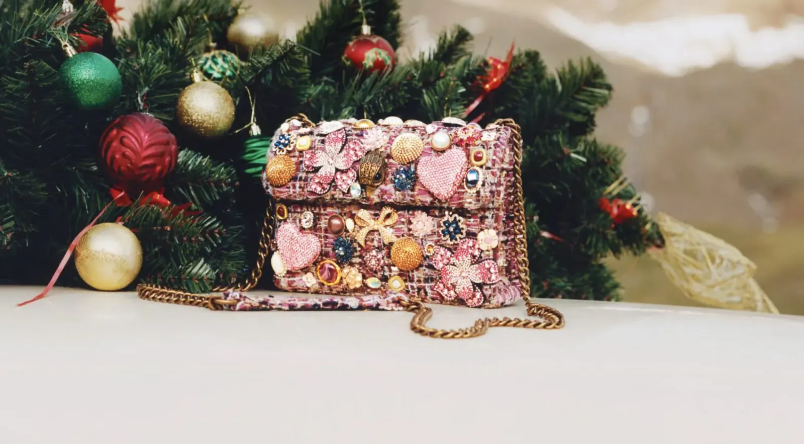 Pink beaded heart handbag with pearls and sequins on white surface amid Christmas tree ornaments and snowy mountains