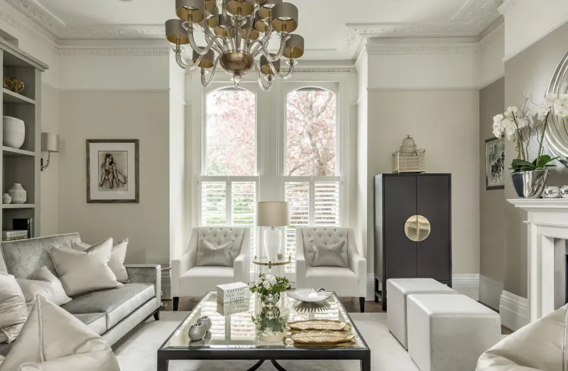 Elegant living room with cream sofa, armchairs, glass coffee table, chandelier, orchids, and garden-view windows.