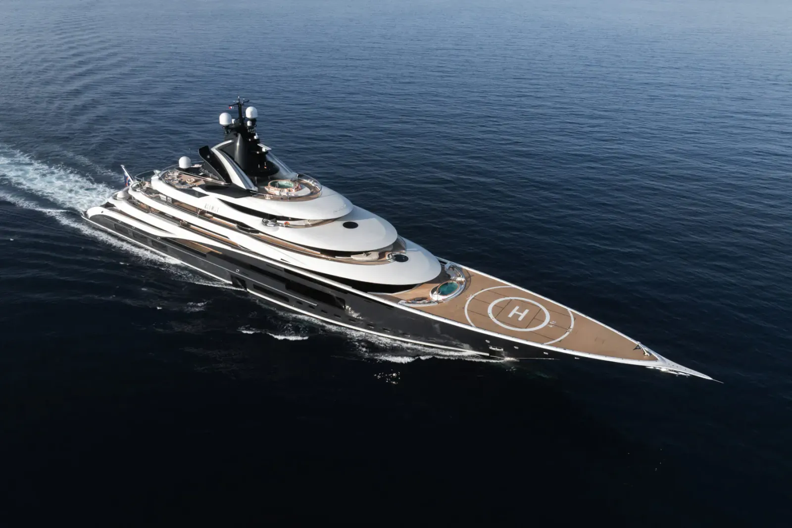 Luxury yacht Kismet speeding across blue ocean, sleek black and white design with H helipad on deck.