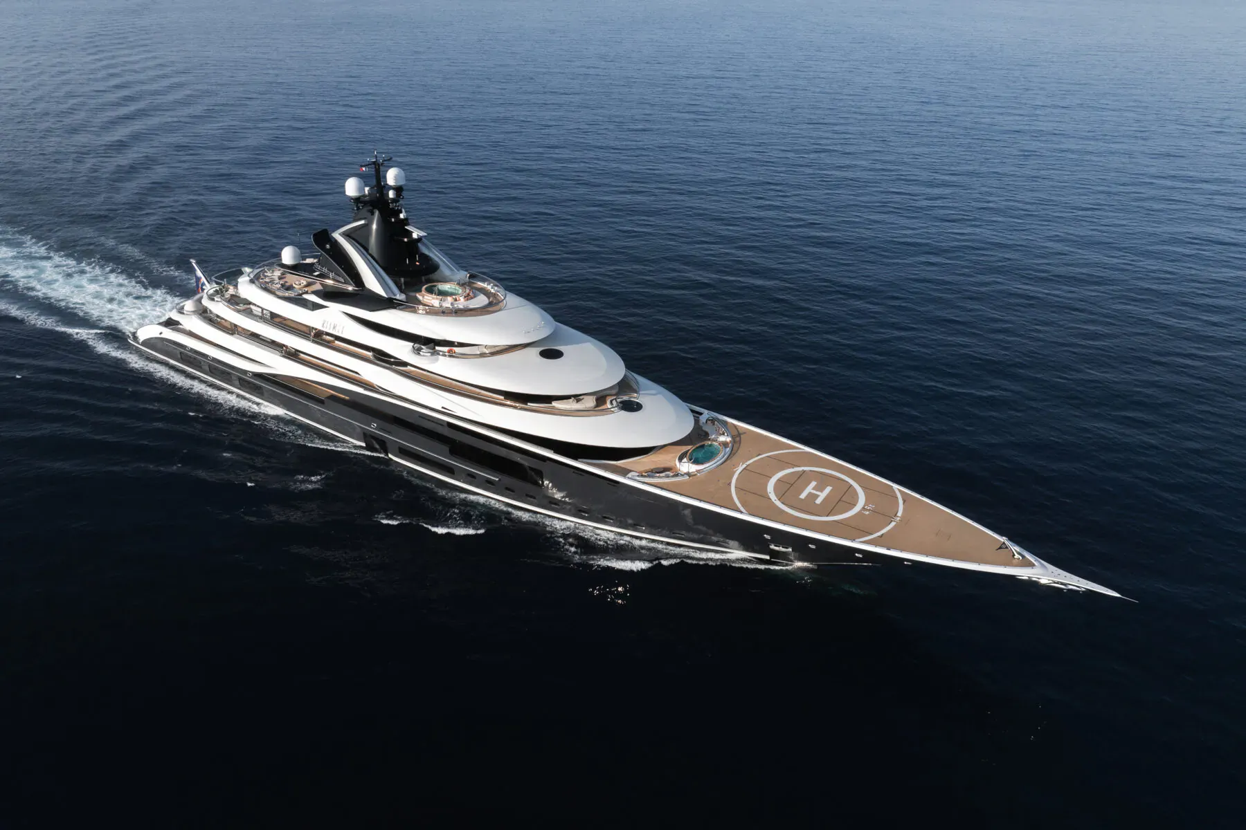 Luxury yacht Kismet speeding across blue ocean, sleek black and white design with H helipad on deck.