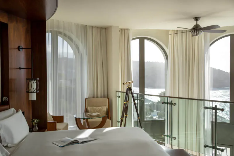 Luxurious Jumeirah Port Soller Hotel suite with king bed, armchair, telescope, and sea view balcony.