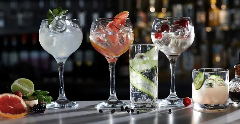 Variety of garnished gin and tonic cocktails on bar counter with limes, grapefruit, and herbs