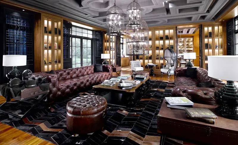 Luxurious hotel lounge at The Sanchaya with oxblood leather sofas, chandeliers, wood cabinets, and patterned rug.