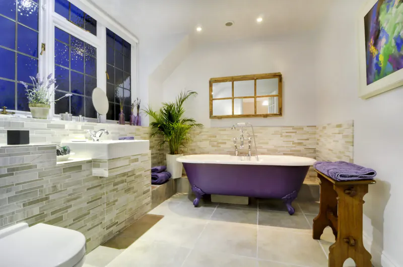 Luxurious bathroom in Bray Cottage with freestanding purple bathtub, vanity, plants, and wooden stool