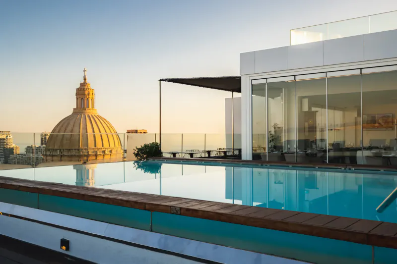 Rooftop pool at Embassy Valletta Hotel with Mosta Dome in background at sunset.