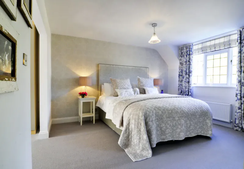 Luxurious bedroom in Bray Cottage with king bed, blue floral curtains, lamps, and artwork.