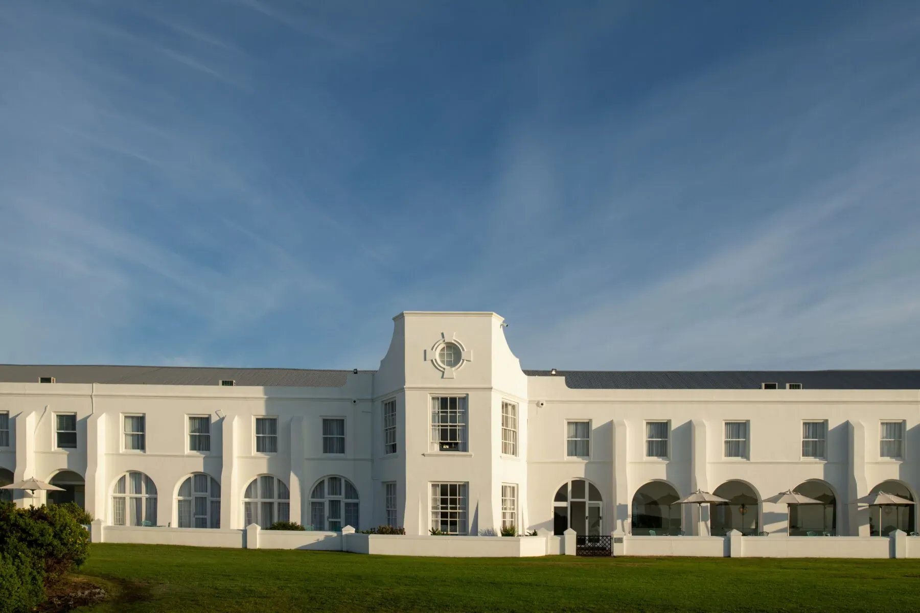 The Marine luxury hotel, white colonial building with clock tower, arches, and lawn under blue sky, South Africa.