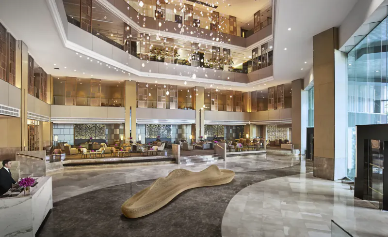 Spacious multi-level Amari Bangkok hotel lobby with chandelier, curved sculpture, seating areas, and glass walls.
