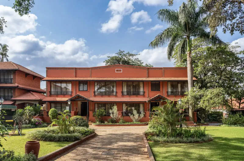 Fairmont The Norfolk, Nairobi: Elegant red brick hotel facade with palm trees, gardens, and driveway under blue sky.