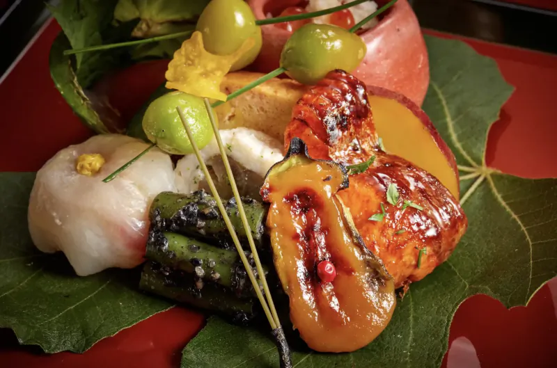 Kaiseki dish on red plate with persimmon leaf: glazed salmon, shrimp, asparagus, cherry tomatoes, garnishes