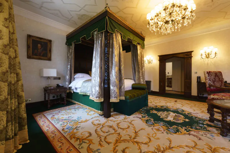 Luxurious bedroom at Thornbury Castle with ornate green four-poster bed, chandelier, and antique furnishings.