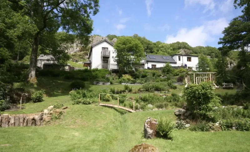 Luxury white holiday cottages nestled in lush green gardens and wooded hillside under blue sky