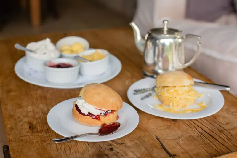 Cream tea on wooden table: scones with clotted cream and jam, butter, silver teapot at Walkersons Hotel.