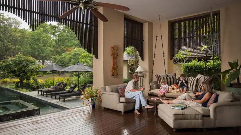 Family relaxing on lounge sofa in luxurious tropical resort villa with pool and garden view